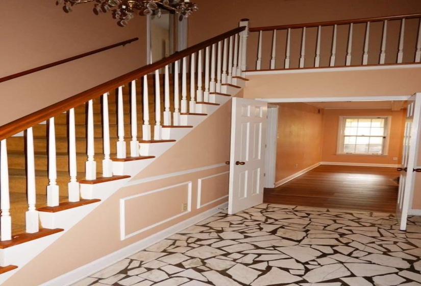 Foyer featuring a custom mosaic-style tile floor, a staircase with wood-finish handrails and white balusters, and decorative wall molding