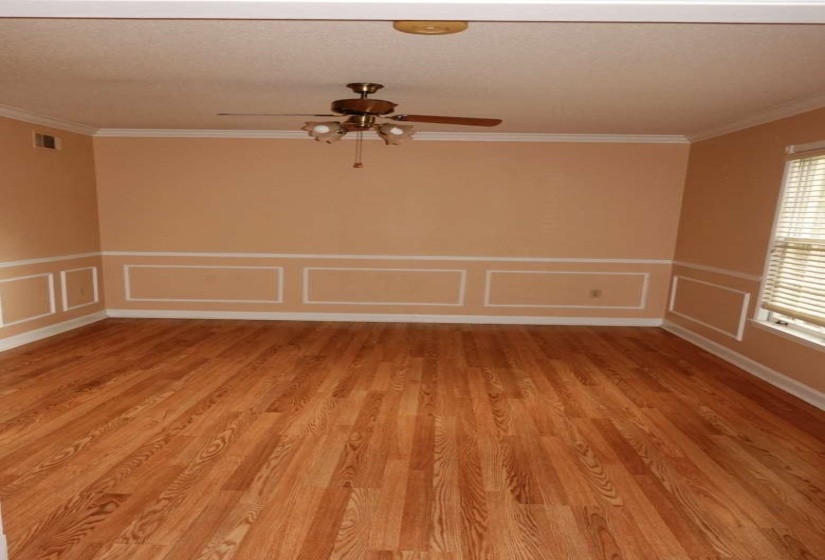 Room featuring wood-finish flooring, wainscoting with decorative trim, and crown molding