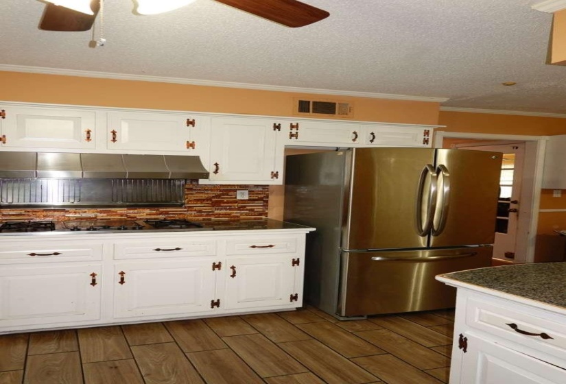 Kitchen featuring white cabinetry with dark hardware, a stainless steel refrigerator, a built-in cooktop, and a mosaic tile backsplash