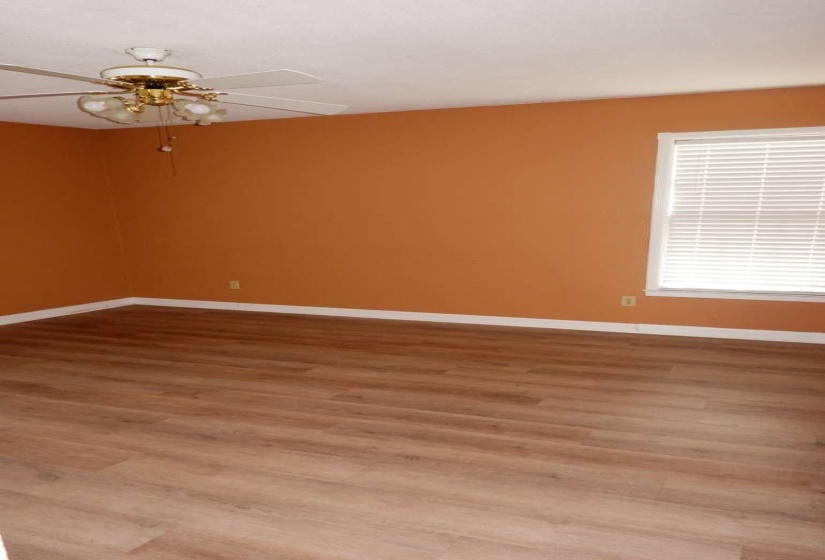 Spacious room featuring wood-finish flooring, white baseboards, and a window with blinds