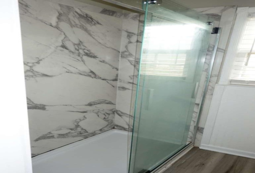 Walk-in shower featuring a sliding glass door enclosure and white-and-gray patterned wall panels