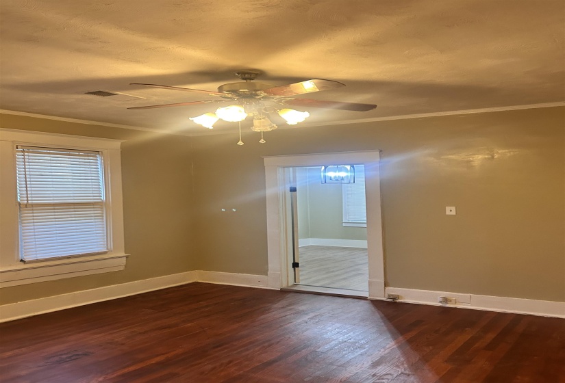 Empty room with dark wood-style floors, ornamental molding, and ceiling fan