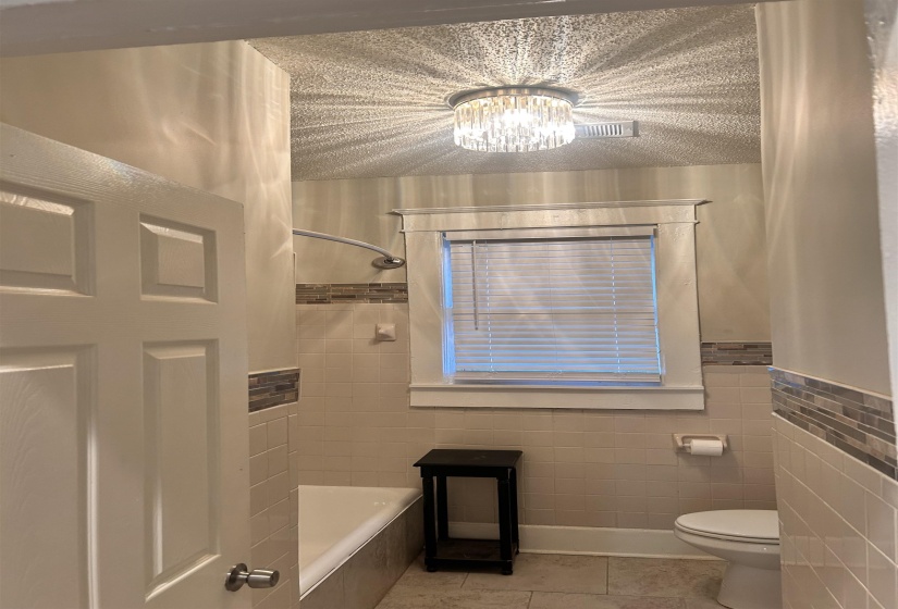 Full bath with light tile patterned floors, tiled shower / bath combo, tile walls, and a chandelier