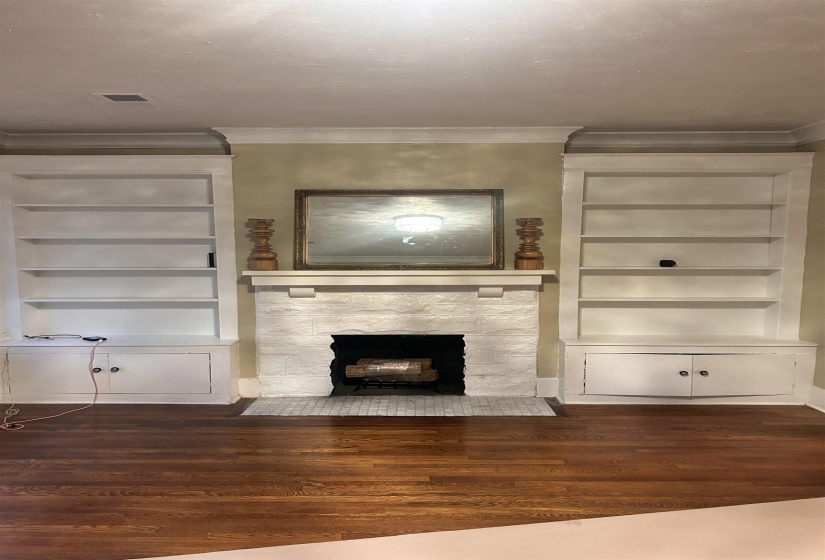 Unfurnished living room featuring built in features, a stone fireplace, crown molding, and dark wood-style floors