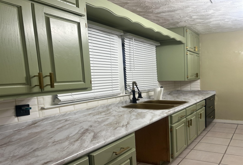 Kitchen featuring green cabinetry, backsplash, and light tile patterned flooring