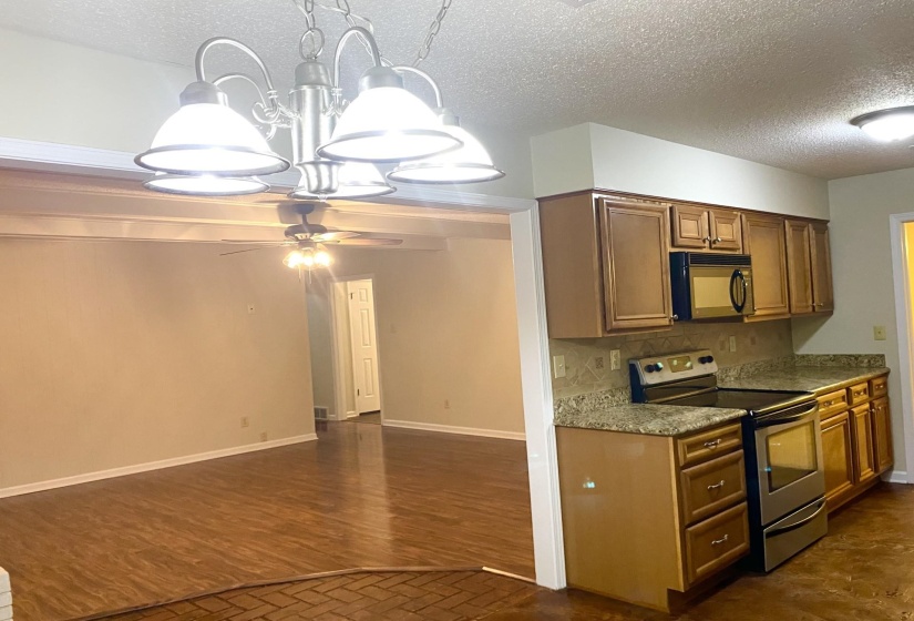 Kitchen with ceiling fan with notable chandelier, tasteful backsplash, dark wood-type flooring, a textured ceiling, and stainless steel electric range