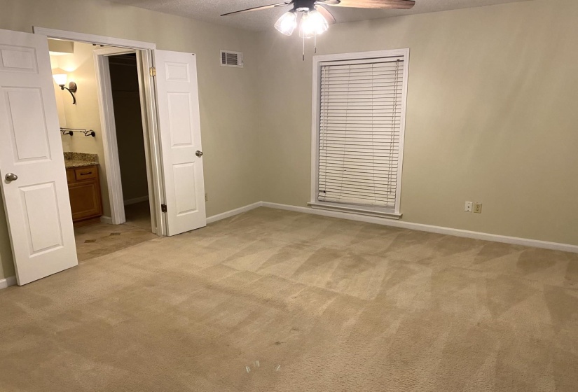 Unfurnished bedroom featuring connected bathroom, a textured ceiling, light colored carpet, and ceiling fan