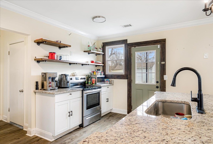 Kitchen featuring stainless steel appliances, white cabinetry, light stone countertops, light wood-type flooring, and crown molding