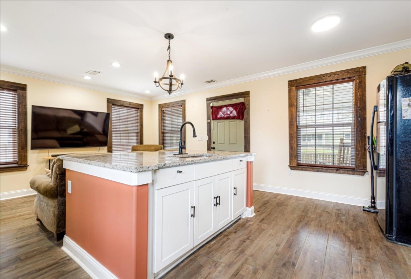 Kitchen featuring freestanding refrigerator, light stone countertops, a center island with sink, white cabinets, and dark wood-style floors