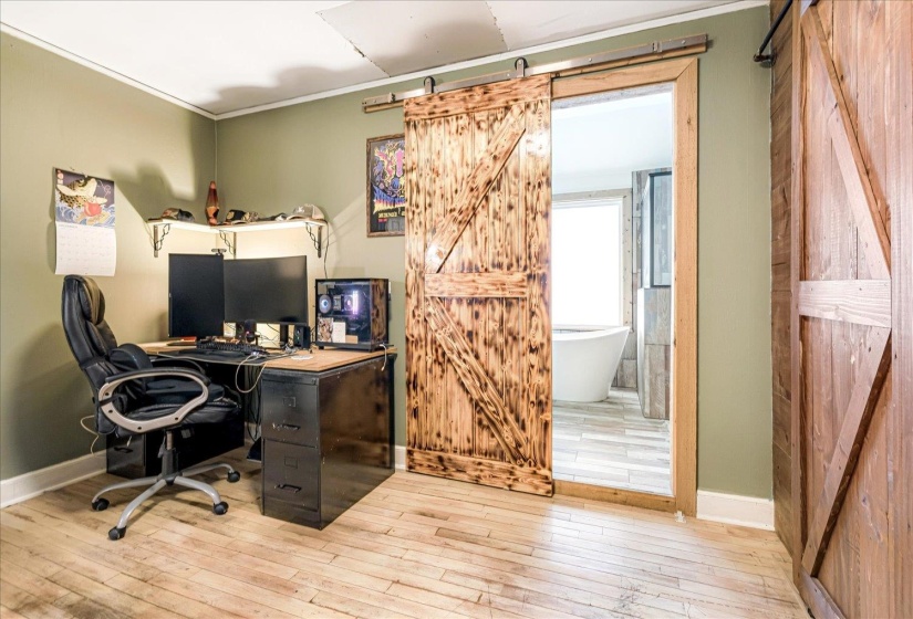 Office space featuring a barn door, wood-type flooring, and ornamental molding