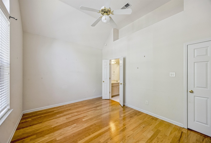 Spacious room featuring vaulted ceilings, wood-finish flooring, a ceiling fan, and window blinds