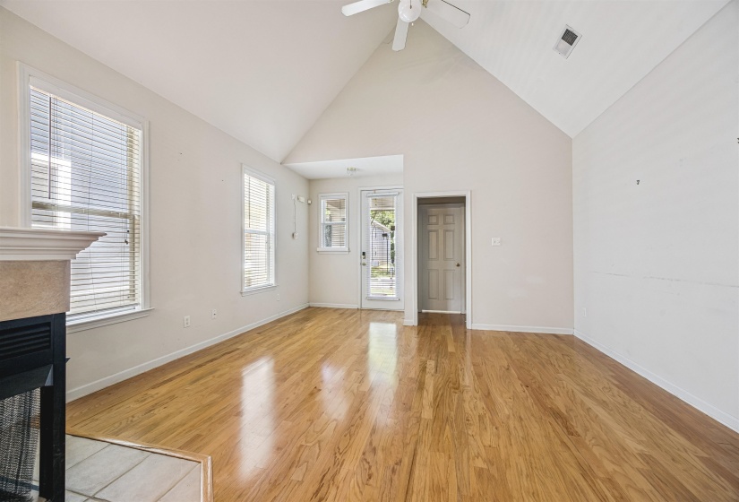 Vaulted ceiling living area featuring wood-finish flooring, a ceiling fan, a fireplace with a stone-finish hearth, and a glass-paneled door