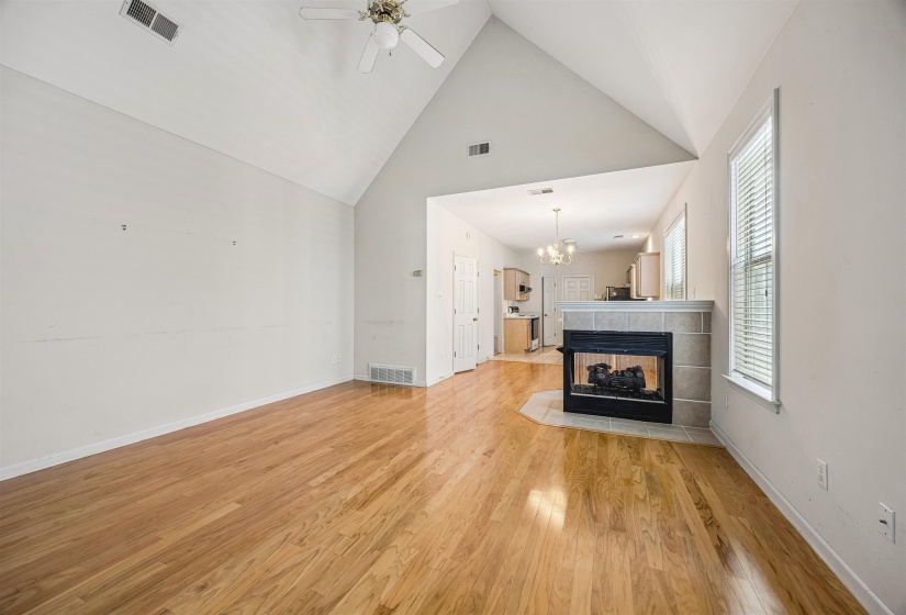 Living area featuring wood-finish flooring, a tiled fireplace with hearth, a vaulted ceiling with a ceiling fan, and a window with blinds
