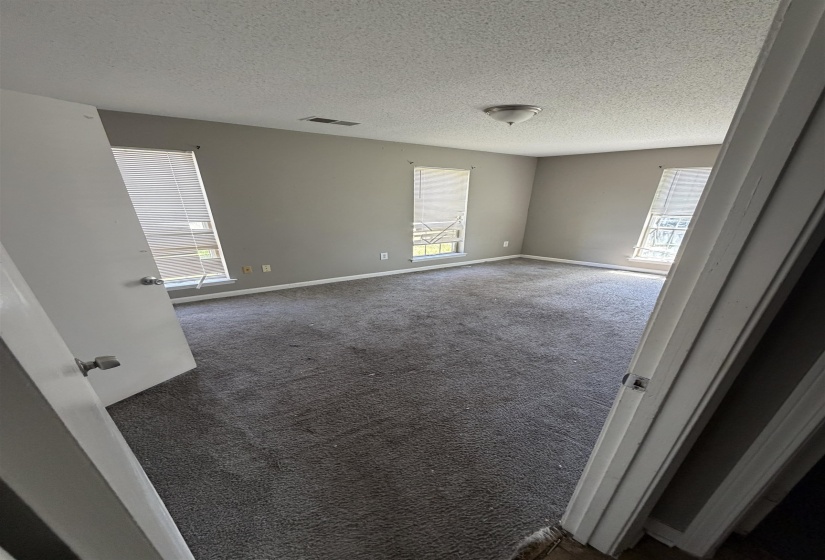 Spacious interior room featuring neutral gray walls, textured ceiling, and gray carpet