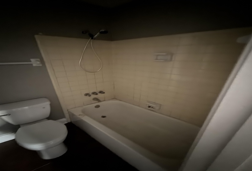 Bathtub-shower combination featuring cream-toned tiled walls and a handheld showerhead