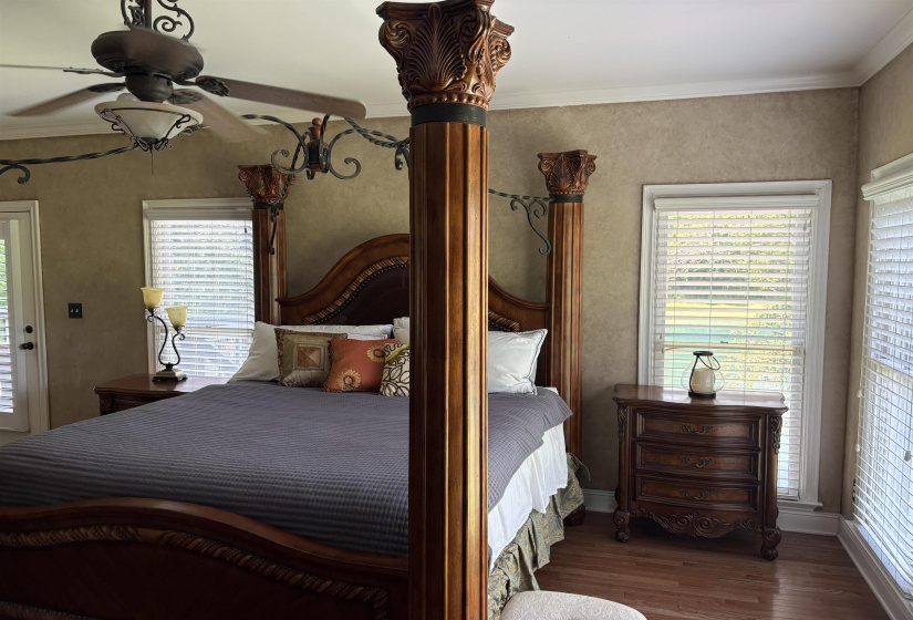 Spacious room featuring wood-finish flooring, two windows with blinds, a ceiling fan with integrated lighting, and a door with louvered panels