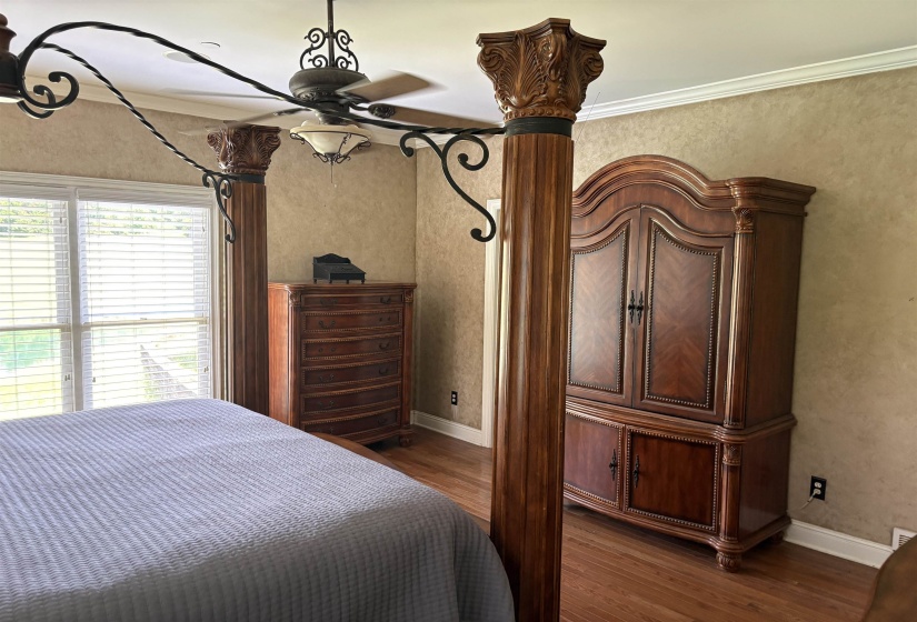 Hardwood-finish flooring featuring a multi-pane window with horizontal blinds, textured wall finishes, crown molding, and a ceiling fan with integrated lighting