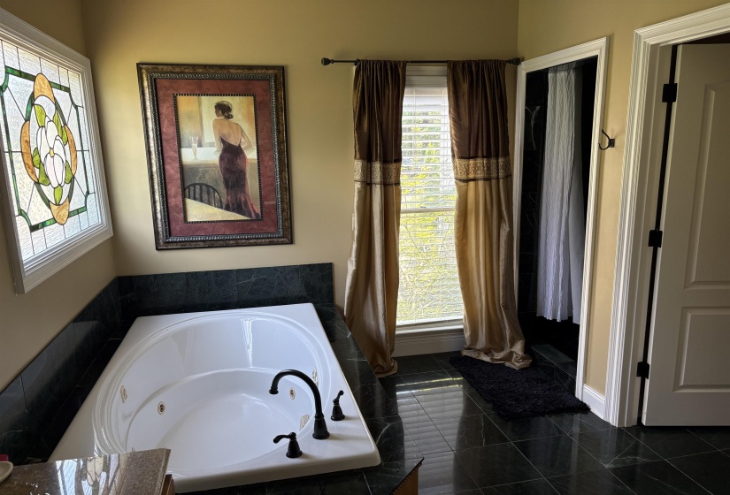 Soaking tub featuring a dark bronze faucet, dark green stone surround, and dark green tile flooring