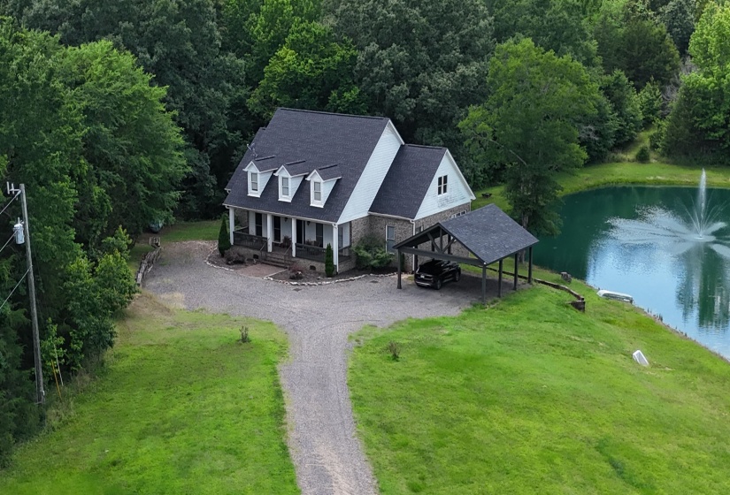 Gable-style home featuring a gravel driveway, covered front porch, an attached carport, and a prominent pond with a water feature