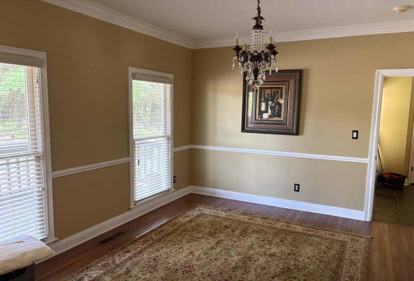 Room featuring crown molding, chair rail detailing, wood-finish flooring, a crystal chandelier, and multiple windows