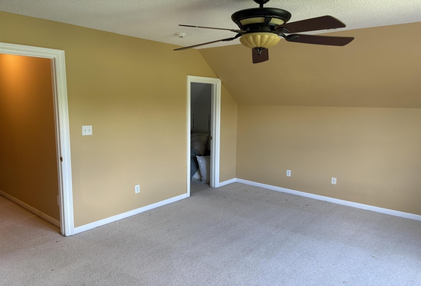 Carpeted room featuring a ceiling fan with integrated lighting, two doorways, and sloped ceiling details