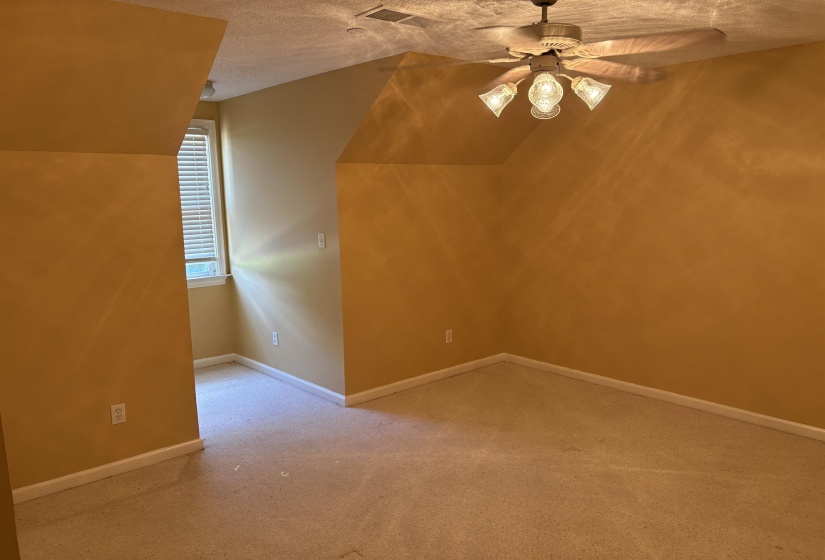 Carpeted room featuring a ceiling fan with integrated lighting, a window with blinds, and angled ceiling lines