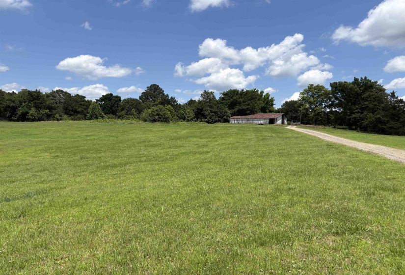 Expansive green field with a gravel driveway leading to a white outbuilding featuring a corrugated metal roof