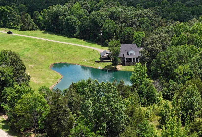Expansive property featuring a private pond with a central fountain, surrounded by mature trees and verdant landscaping