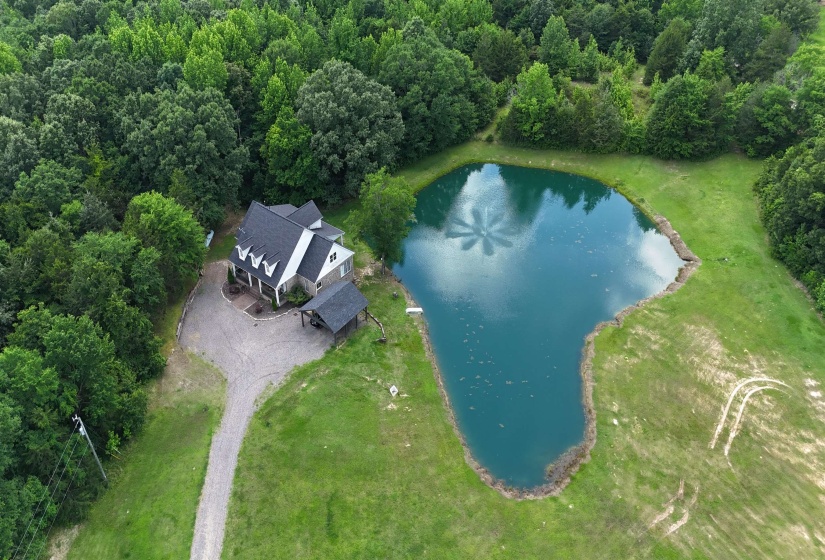 Property featuring a private pond, gravel driveway, and surrounding mature trees