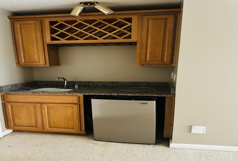 Built-in wet bar featuring wood cabinetry, integrated wine storage, granite-finish countertop, and stainless steel compact refrigerator