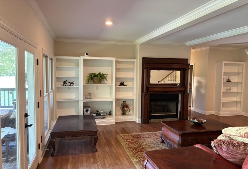 Hardwood flooring throughout featuring built-in white shelving, a dark wood fireplace with an integrated mirror, and crown molding