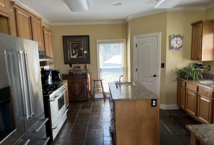 Kitchen featuring stainless steel appliances, wood cabinetry, granite countertops, and dark tile flooring