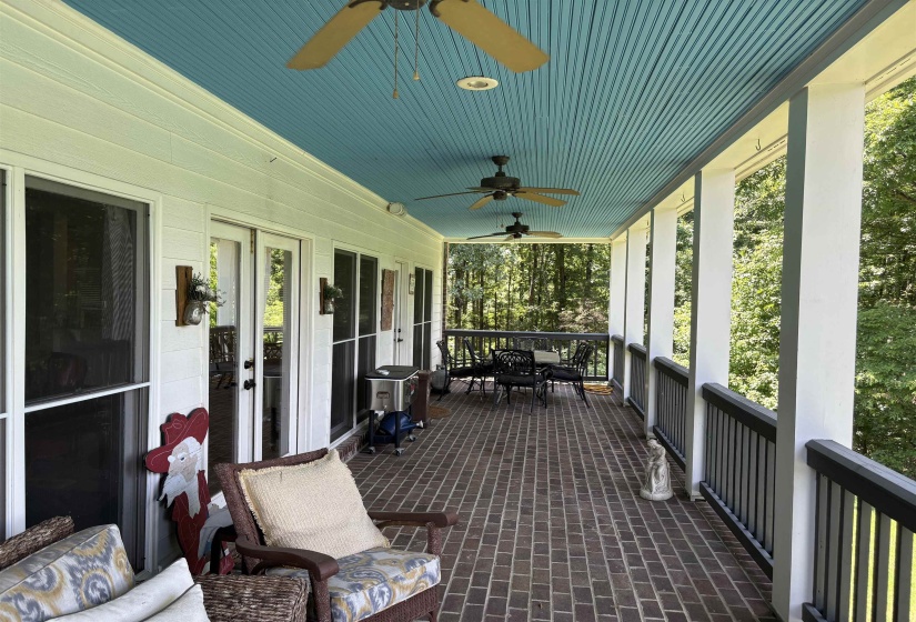 Expansive covered porch featuring a brick-patterned floor, a light blue beadboard ceiling