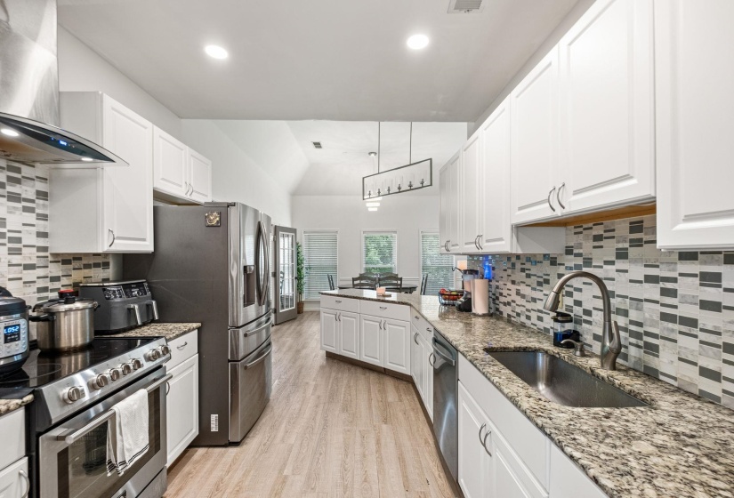 Modern kitchen featuring white cabinetry, stainless steel appliances, speckled stone countertops, and a tiled backsplash