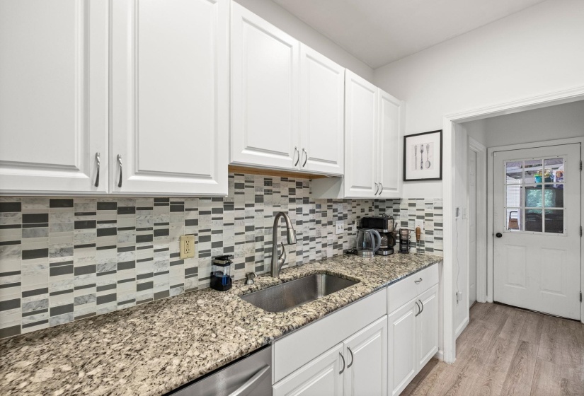 Kitchen featuring white shaker-style cabinetry, a stainless steel sink with a gooseneck faucet, light-toned granite countertops, and a patterned tile backsplash