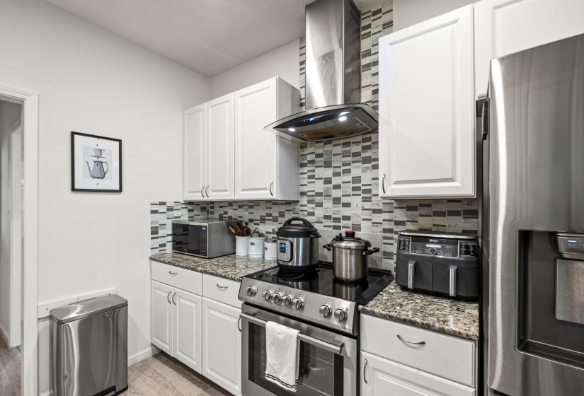 Kitchen featuring white shaker cabinetry, stainless steel appliances, granite countertops, a mosaic tile backsplash, and wood-finish flooring