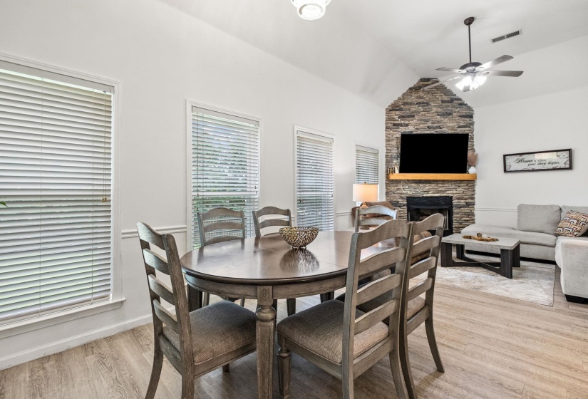 Open-concept living space with vaulted ceilings, a stacked stone fireplace with a wood mantel, and wood-finish flooring