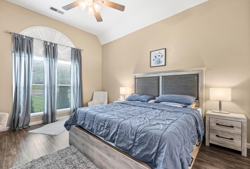 Spacious room featuring vaulted ceilings, wood-finish flooring, and a prominent arched window with vertical blinds