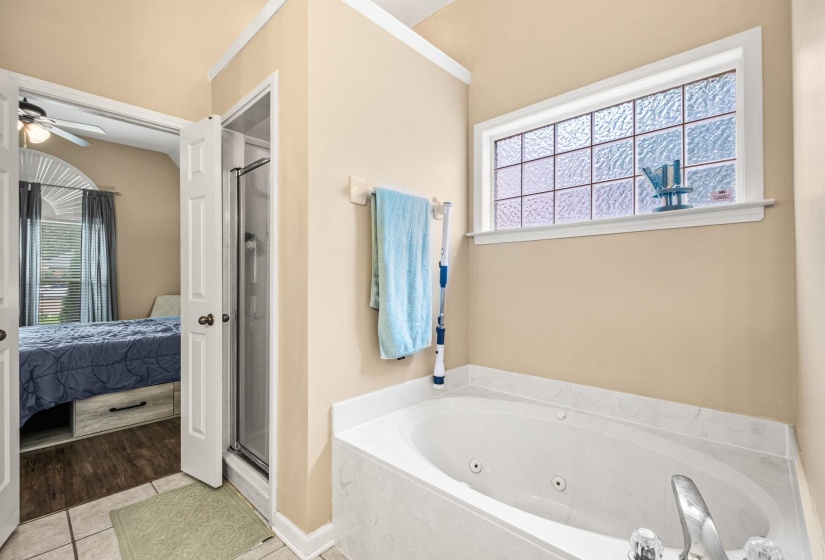 Jetted soaking tub with a tiled surround, frosted glass window, and a separate glass-enclosed shower