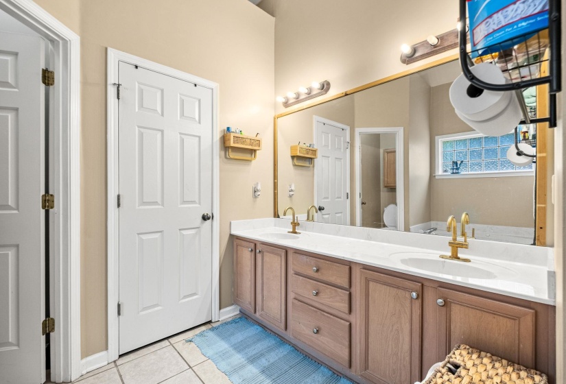 Dual sink vanity with white countertops, warm wood-finish cabinetry, and gold-tone fixtures