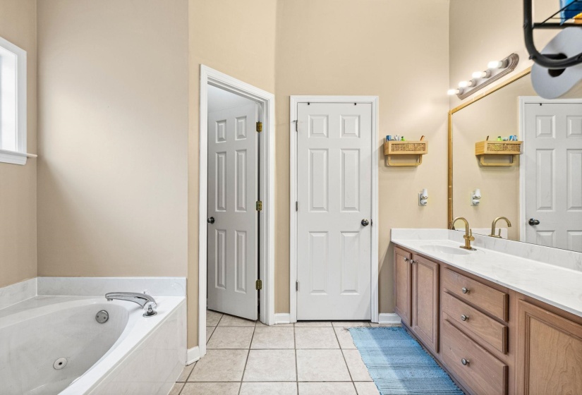 Bathroom featuring a built-in jetted tub, a double vanity with light-toned countertops, wood-finish cabinetry, and tiled flooring