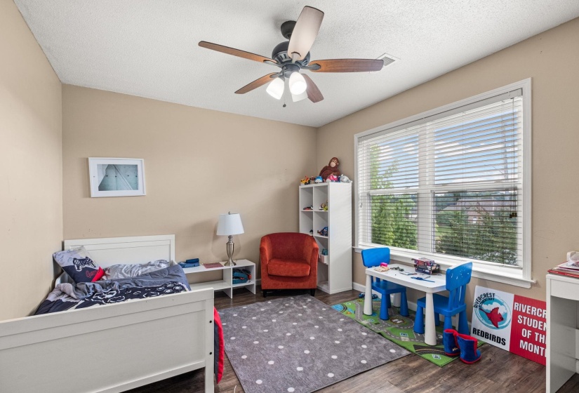Room featuring wood-finish flooring, a ceiling fan with integrated lighting, and a large window with blinds