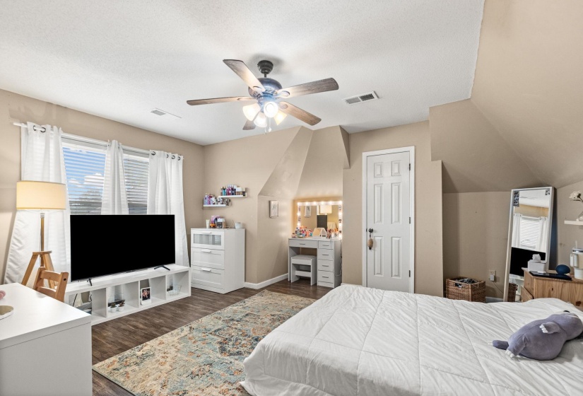 Spacious room featuring wood-finish flooring, light tan walls, and a multi-speed ceiling fan with integrated lighting