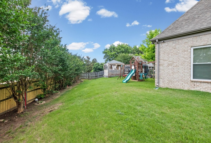 Expansive rear yard featuring green lawn, mature perimeter plantings, new wood fencing, and a light brick exterior with a traditional roofline