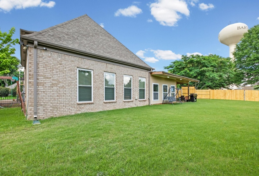 Expansive green lawn with a covered patio, featuring a brick exterior and a privacy fence