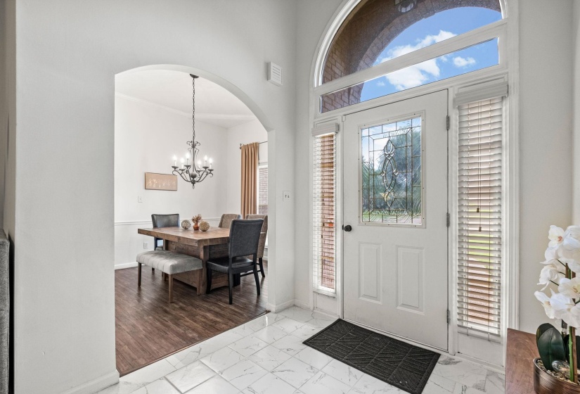 Foyer with white paneled door featuring decorative glass insert, flanked by sidelights with blinds, and topped with an arched transom window