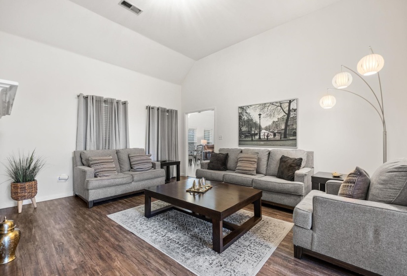 Spacious living area featuring wood-finish flooring, vaulted ceilings, and white walls
