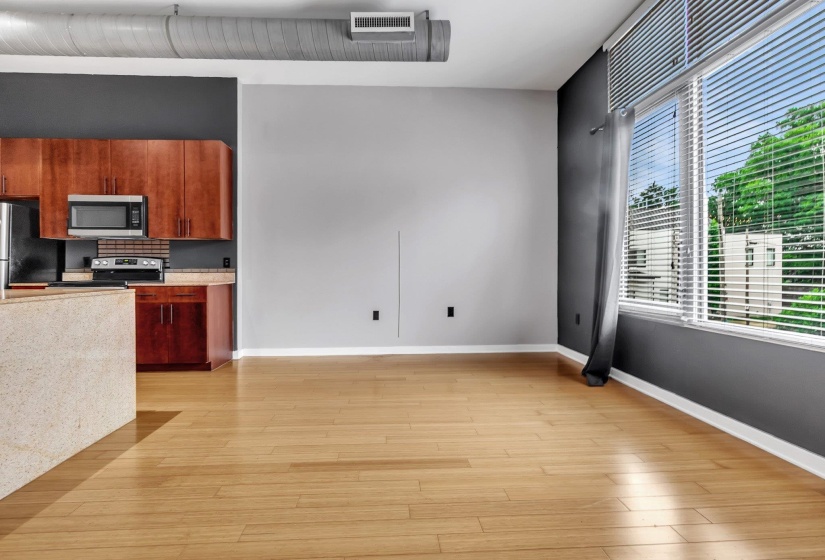 Open-concept living space featuring wood-finish flooring, a kitchen with wood cabinetry and stainless steel appliances, and large windows with horizontal blinds