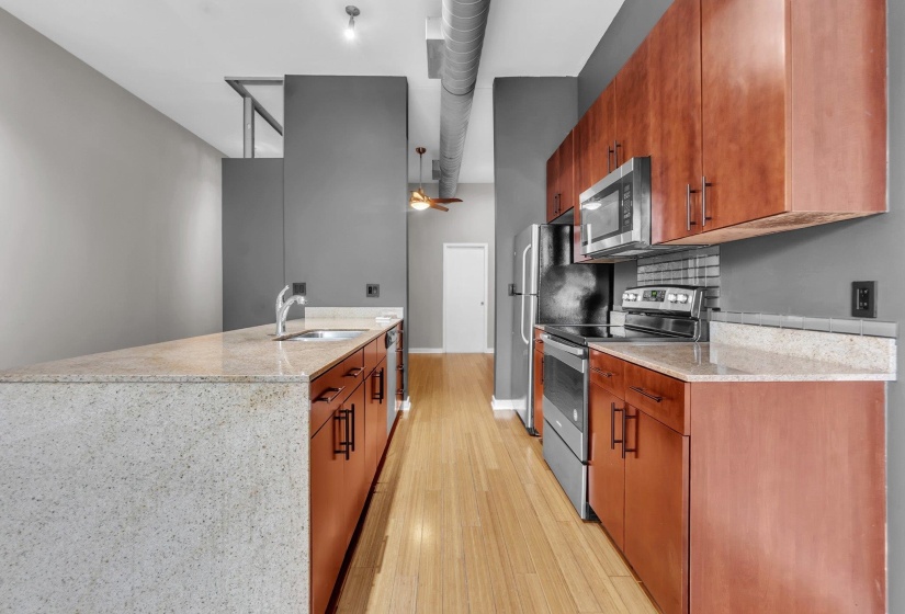 Kitchen featuring wood-finish cabinetry, stainless steel appliances, light-toned countertops, a full-size sink, and wood-finish flooring
