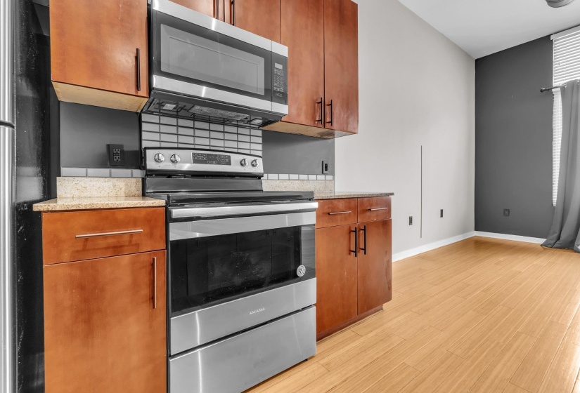 Kitchen area featuring stainless steel appliances, warm wood-finish cabinetry, a tiled backsplash, and light-toned countertops